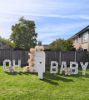 Lichtbakletters OH BABY in de tuin bij gender reveal backdrop